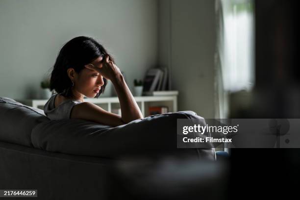 young asian woman sitting on sofa at home feeling sad tired and worried suffering depression in mental health. - psychische-aandoening stockfoto's en -beelden