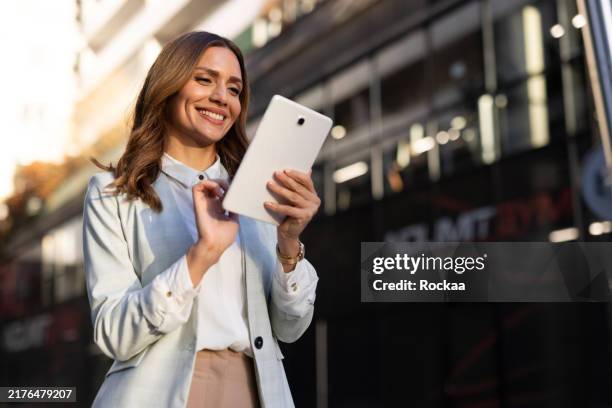 mujer de negocios de pie al aire libre, concentrada en su tableta - oficio financiero fotografías e imágenes de stock