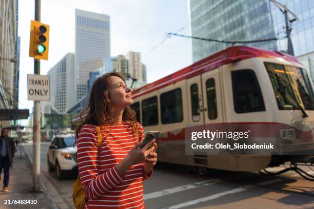 woman using smartphone waiting for the tramway in downtown - calgary stock pictures, royalty-free photos & images
