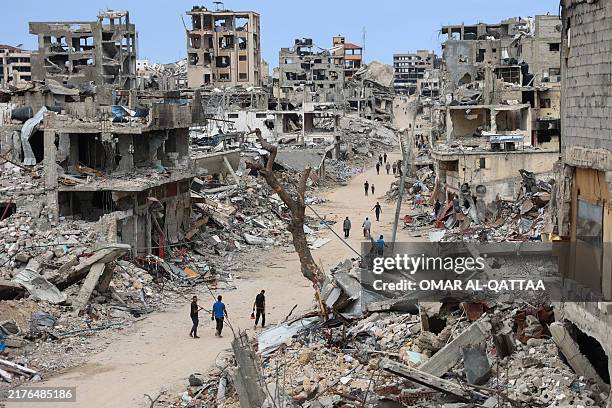 Palestinians walk on a dirt road lined with building rubble in the Shujaiya neighbourhood of Gaza City on October 7 on the first anniversary of the...