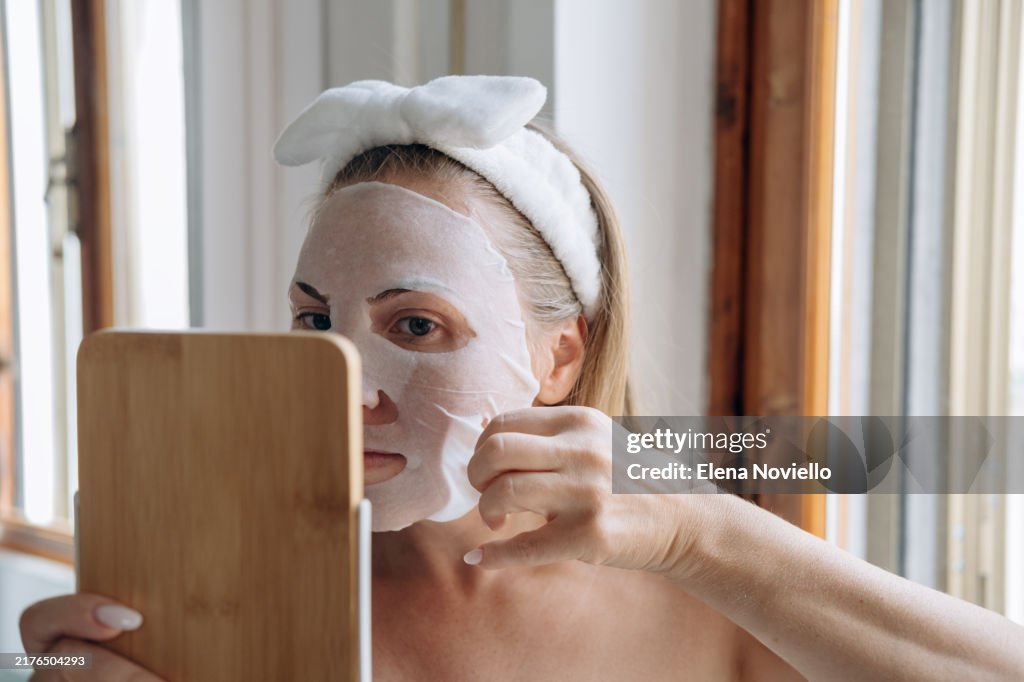Facial skin care woman applies moisturizing facial tissue mask with lifting effect , sheet mask with lifting and anti-age active ingredients