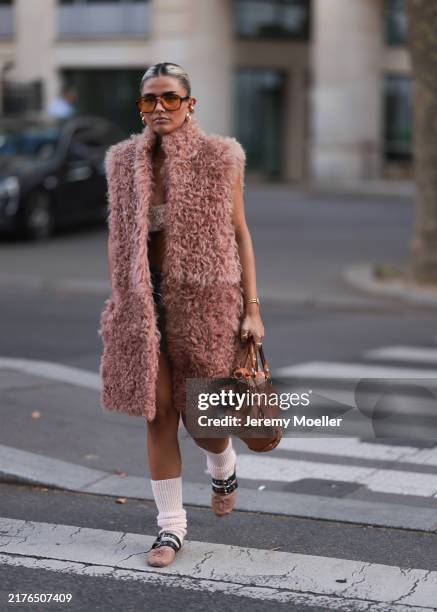 Fashion Week guest is seen wearing aviator sunglasses with a Havana frame and orange lenses, several chunky gold hoop earrings and small ear studs, a...