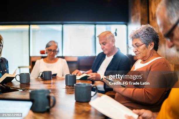 senior woman reading a book at book club on a coffee shop - community center stock pictures, royalty-free photos & images