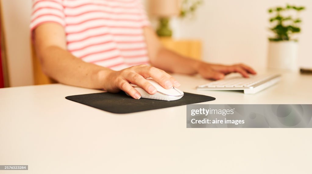 Close-up side view of a woman's hand using her computer mouse, in casual clothes sitting in her home office