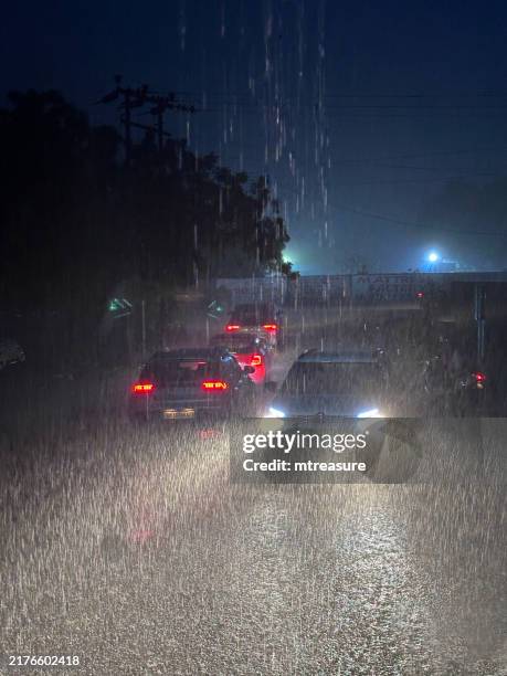 image of car and motorbike with lights on driving through puddles, traffic driving on wet road, water wake, splashes and spray, flooded road surface, vehicles driving in monsoon season at night - rainy season stock pictures, royalty-free photos & images