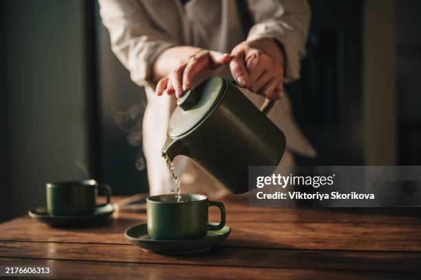 tea is poured from a green teapot into matching mugs - tasse à thé photos et images de collection