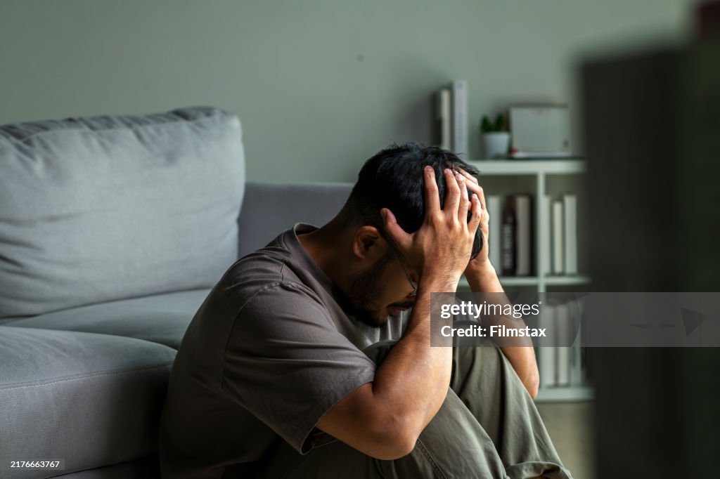Young Asian man sitting on floor feeling sad tired and worried suffering depression in mental health.