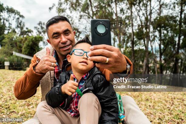 un père prend un selfie avec son fils trisomique à l’extérieur - smartphone thumb up down photos et images de collection