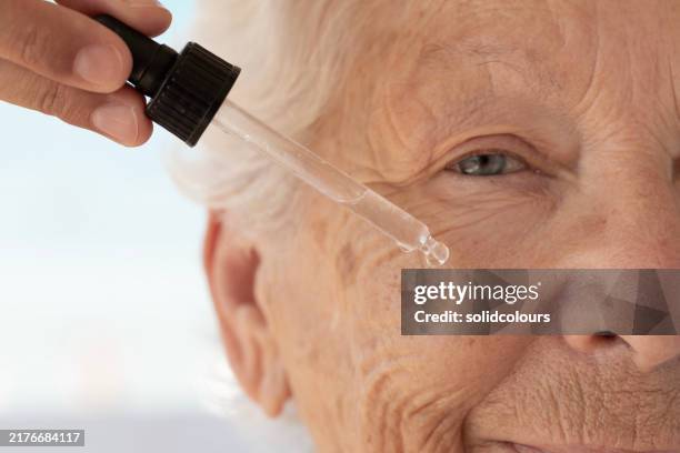 elderly woman skincare routine using dropper - hyperpigmentation stockfoto's en -beelden