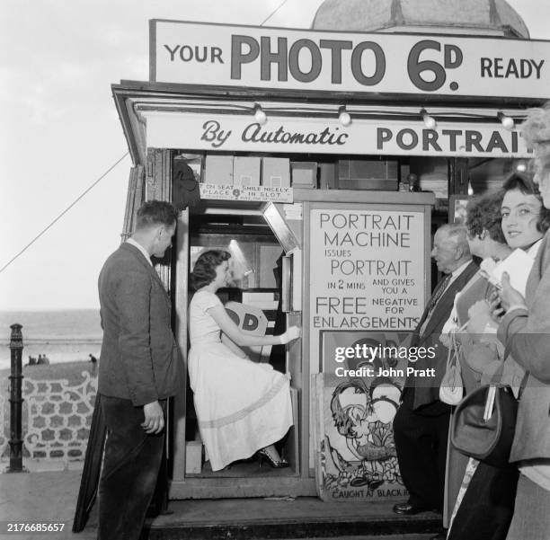 Northern Irish singer Ruby Murray is observed by a small group of admirers as she has her picture taken in a photo booth at Brighton Pier, Sussex,...