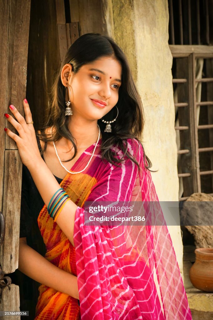 Portrait of happy indian young woman in sari standing near door and contemplating.