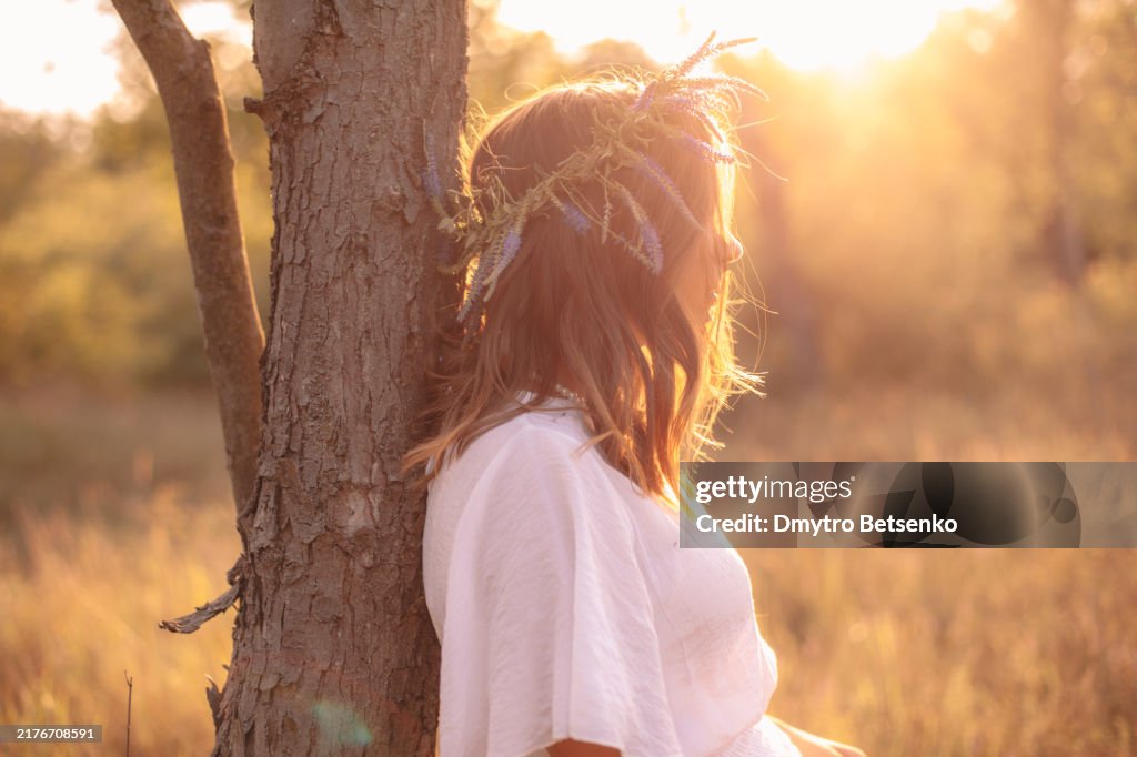 Young woman leaning on a tree while standing in the forest during summer