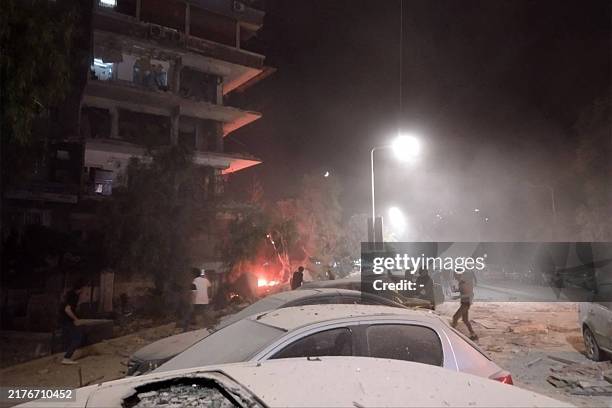 People gather by damaged vehicles at the site of a reported Israeli air strike on a residential building, where reportedly senior members of Iran's...