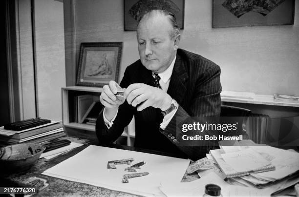 Sotheby's auctioneer Peter Wilson seated at his desk examining an item, London, September 22nd 1962.