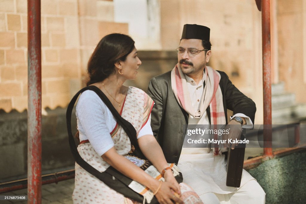 Mid-Adult Indian couple dressed in Retro-Style clothing, sitting at bus stop, waiting for the bus