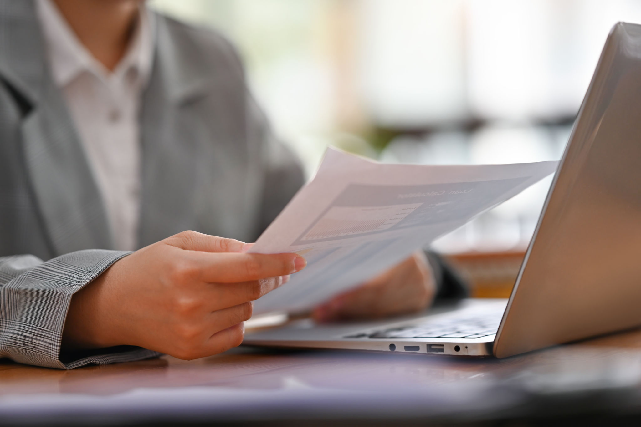 Close up and cropped image of Young businesswoman's hand holding a financial report documents and using laptop. Close up and cropped image of Young businesswoman's hand holding a financial report documents and using laptop.