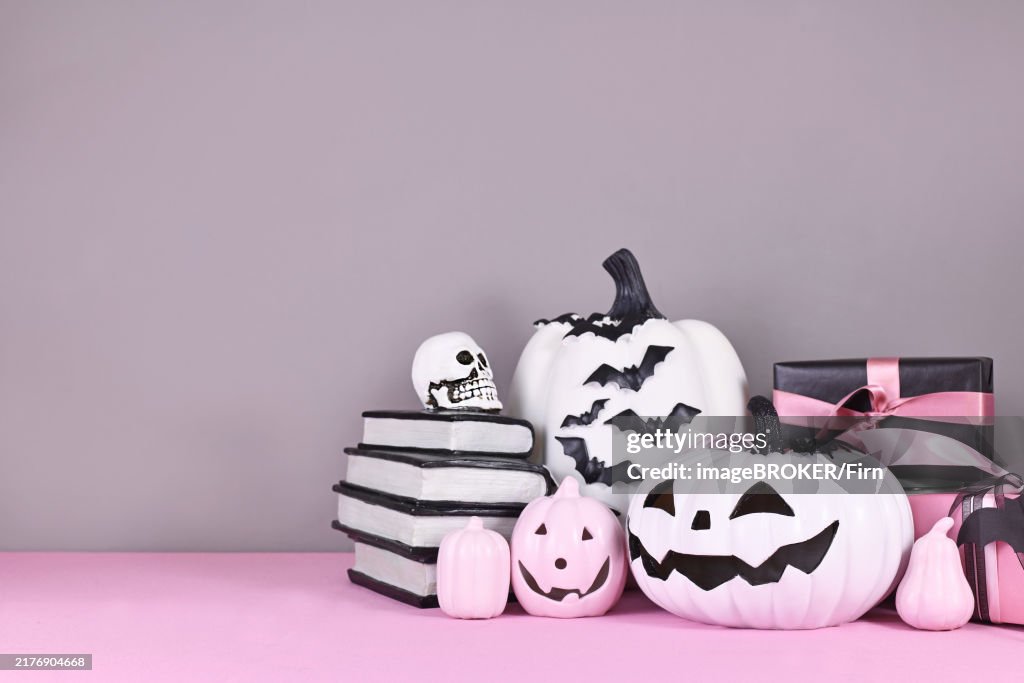 Pink and white Halloween decor with black and white pumpkins, spell books and spiders on gray background with copy space