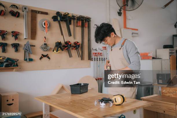 asian chinese young trainee getting ready to work putting on work tool on apron in workshop - workbench stock pictures, royalty-free photos & images