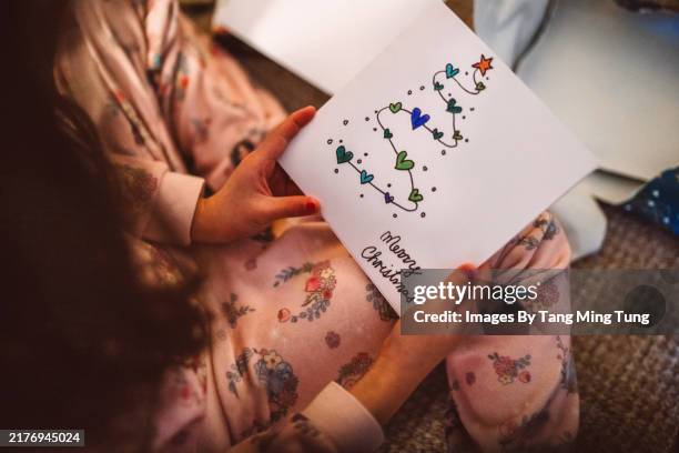 young girl holding a christmas card while unwrapping christmas presents at home on christmas morning - christmas card stock pictures, royalty-free photos & images