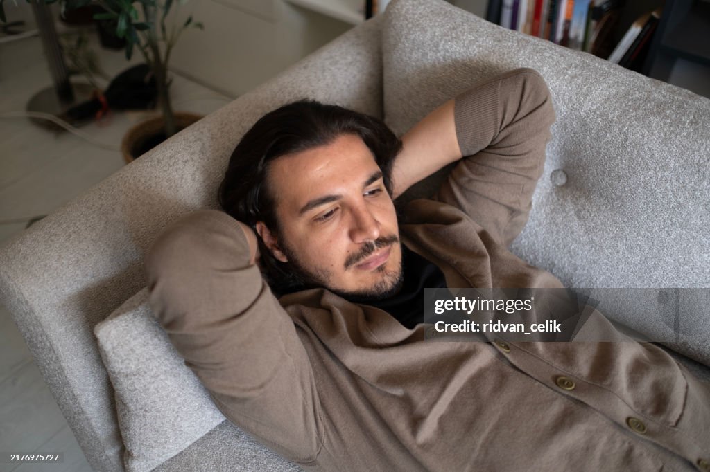 Pensive young man lying on sofa at home