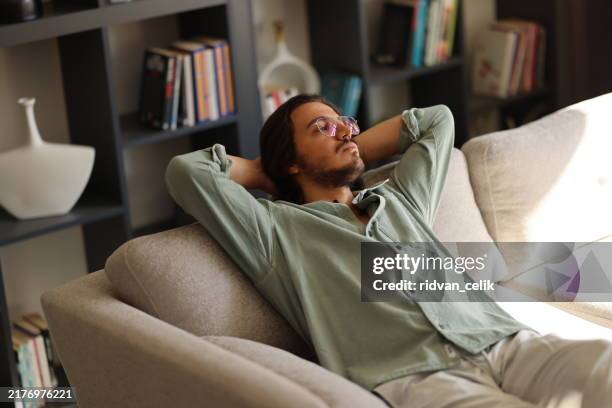 pensive young man lying on sofa at home - young widower stock pictures, royalty-free photos & images