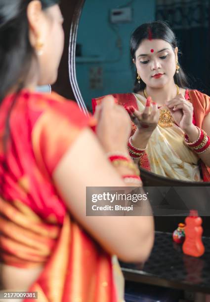 beautiful bengali woman in traditional sari applying alta (red dye) in hand for druga puja festival. - bengali art stock pictures, royalty-free photos & images