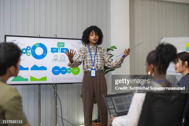 an african businesswoman confidently delivers a presentation in a meeting room to a diverse audience of professionals, showcasing her leadership skills and promoting effective communication in a corporate environment. - slide show presentatiesoftware stockfoto's en -beelden
