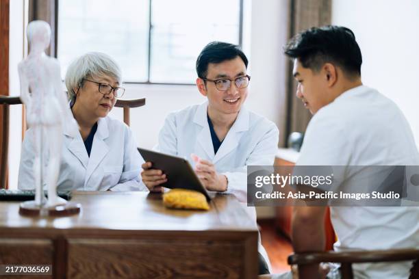 traditional chinese medicine series. two tcm doctors talking and explaining with a young male athlete and using digital tablet to discuss at doctor's office. - chinese herbal medicine stock pictures, royalty-free photos & images