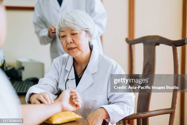 taking pulse. close up of a senior female tcm doctor taking pulse for a young male athlete at doctor's office. traditional chinese medicine series. - chinese herbal medicine stock pictures, royalty-free photos & images
