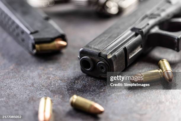 close-up of a black metal 9mm automatic pistol with bullets all placed on a concrete table - bala munición fotografías e imágenes de stock