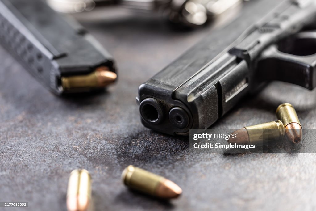 Close-up of a black metal 9mm automatic pistol with bullets all placed on a concrete table