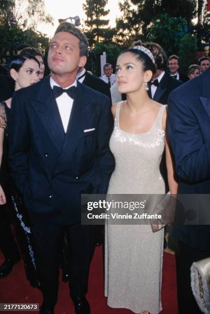 Mexican singer Luis Miguel, wearing a tuxedo and bow tie, and Mexican actress Salma Hayek, who wears a sleeveless scooped-neck sequin dress, attend...