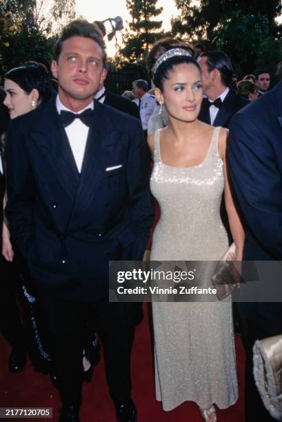 Mexican singer Luis Miguel, wearing a tuxedo and bow tie, and Mexican actress Salma Hayek, who wears a sleeveless scooped-neck sequin dress, attend...