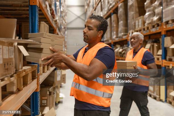 two middle aged multi ethnic male warehouse workers during the daily duties on site - warehouse worker stock pictures, royalty-free photos & images