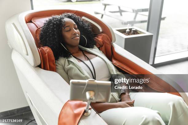 schöne schwarze lagerleiterin, die sich während ihrer täglichen aufgaben auf der baustelle auf einem massagesessel entspannt - massagestuhl stock-fotos und bilder