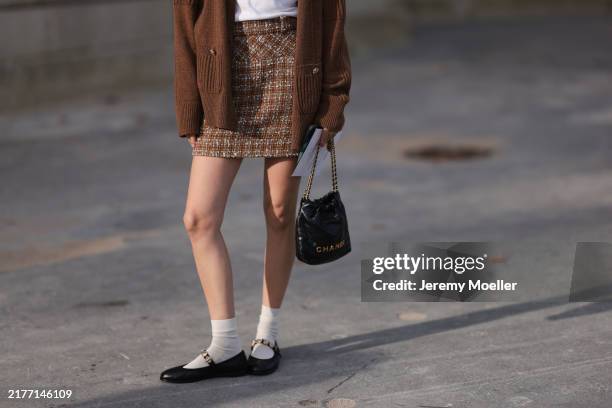 Marie von Behrens is seen wearing a brown plaid skirt, with a white top, a long brown cardigan, white short socks and black ballerinas, with a black...