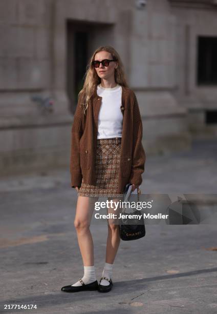 Marie von Behrens is seen wearing a brown plaid skirt, with a white top, a long brown cardigan, white short socks and black ballerinas, with a black...