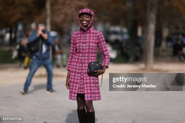 Fashion week guest is seen wearing a pink cap, a pink plaid bouclé long jacket and matching skirt, black high boots with a black Chanel handbag...
