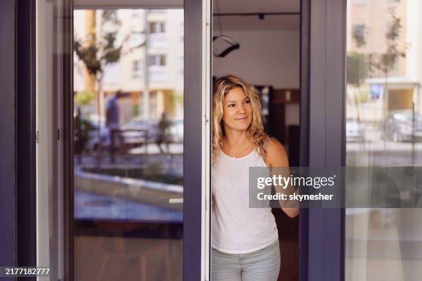 donna sorridente che apre le porte scorrevoli su un patio. - porta scorrevole foto e immagini stock