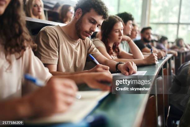 male college student writing an exam in lecture hall. - schulische prüfung stock-fotos und bilder