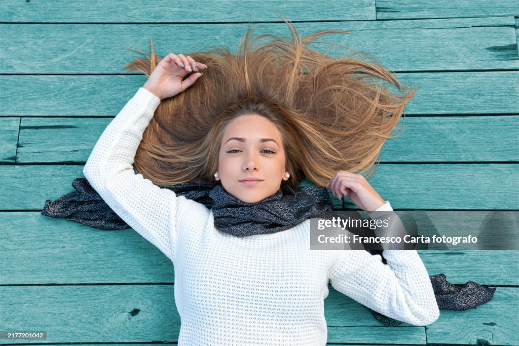 Above view of happy young woman lying down on wooden floor