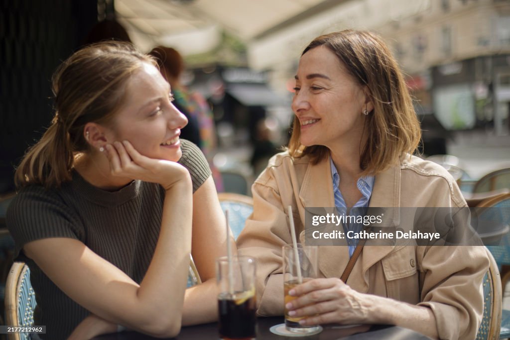 A mother and her 20 year old daughter spending time together on the terrace of a Parisian cafe