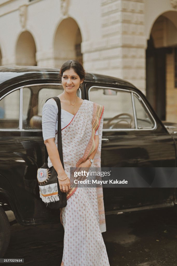 Mid-adult woman in sari leaning against a vintage car