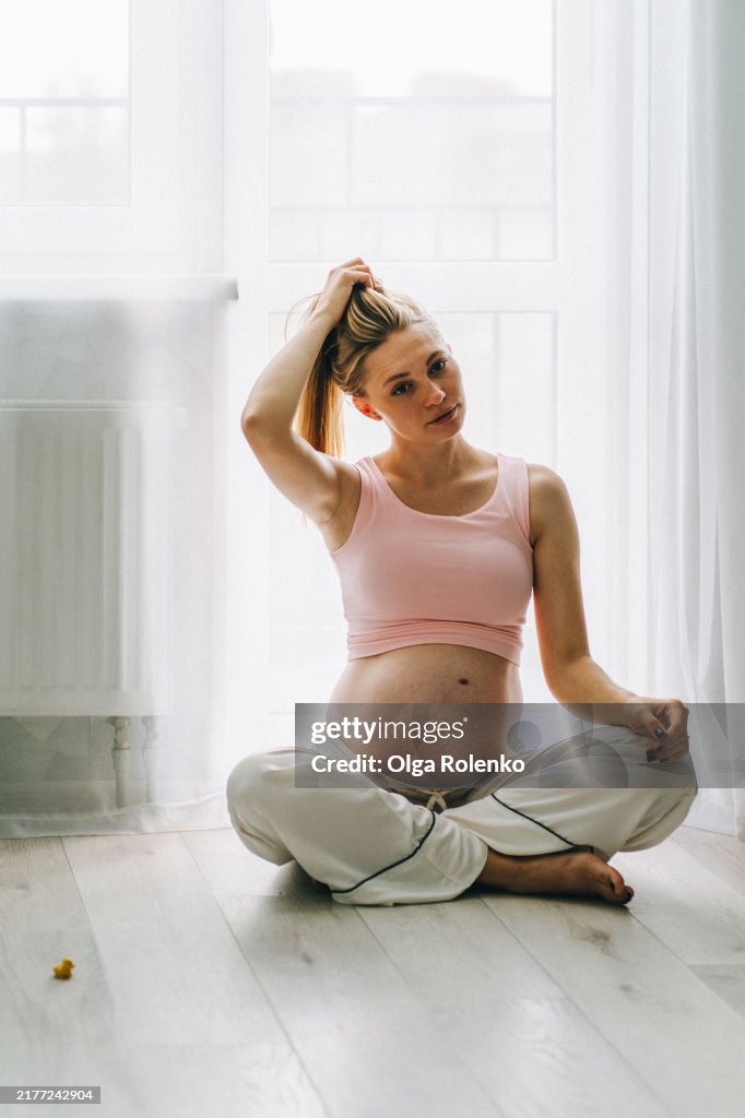 Pregnant woman sitting in lotus pose on the floor at home preparing for breathe exercises
