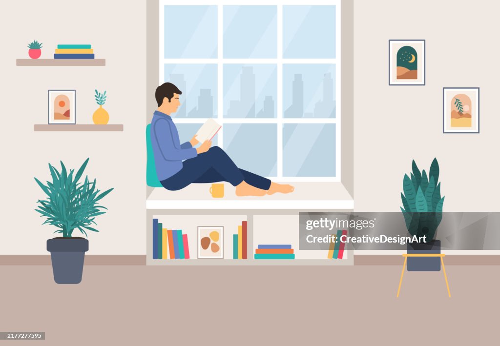 Young Man Sitting On Windowsill And Reading Book. Modern Living Room Interior With Bookshelf, Picture Frames And Houseplants