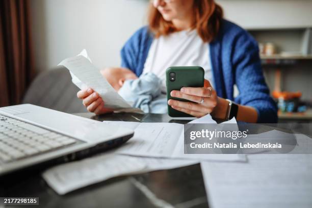 work-life balance - middle-aged mother achieves a balance between work and personal life, dealing with finances and papers while taking care of her newborn - modulo per la dichiarazione dei redditi foto e immagini stock