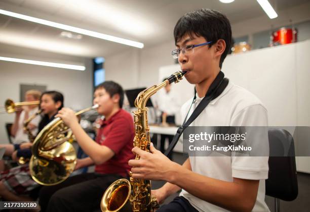 asian chinese teenage boy junior high student playing saxophone in band class in school orchestra - saxophone stock pictures, royalty-free photos & images