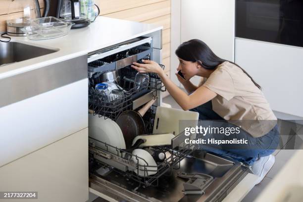 woman at home having a problem with her dishwasher and calling a plumber - dishwasher stockfoto's en -beelden