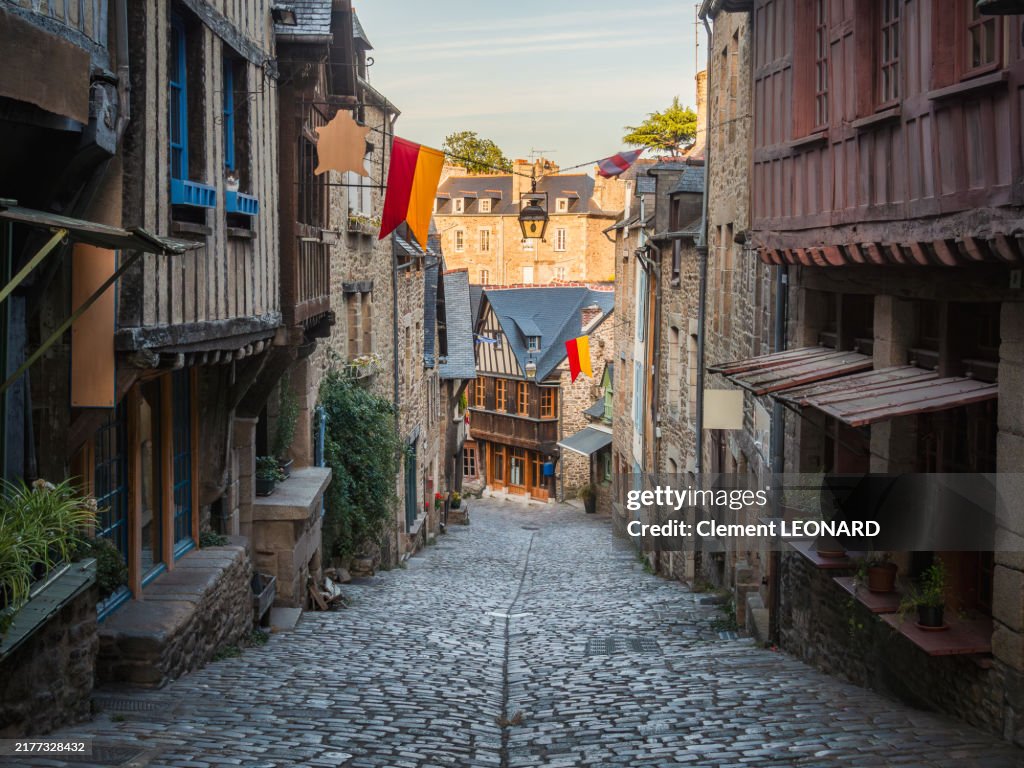 Close-up view of a picturesque cobblestone street in the medieval old town of Dinan at sunset, the Rue du Jerzual, with several traditional colorful half-timbered houses and banners, Cotes-d'Armor - Bretagne (Brittany).