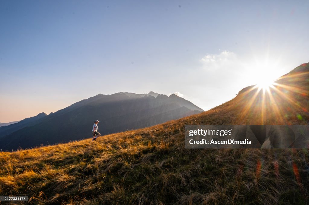 Young woman hikes up mountain meadow at sunrise